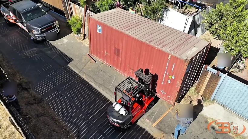 A forklift moving a red shipping container down a driveway, seen from above