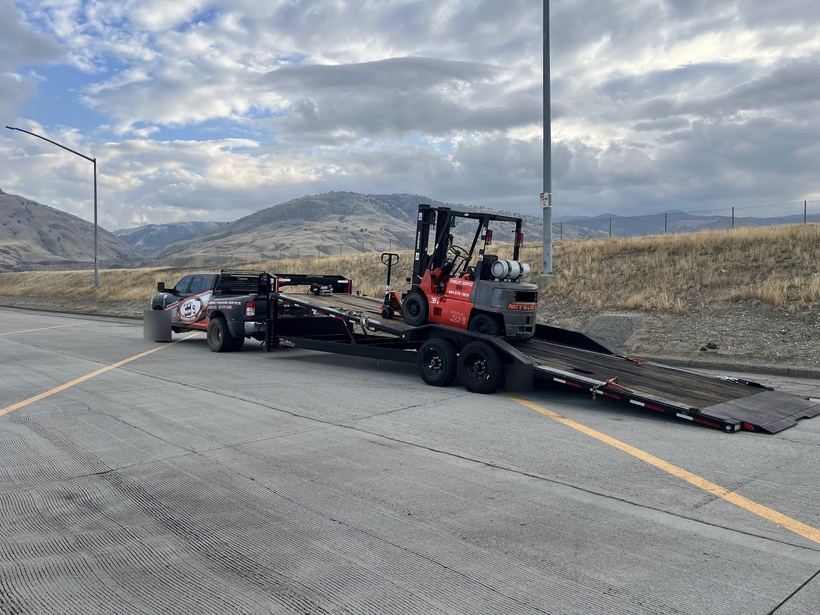 A forklift loaded on the 3B's trailer on a road below dry hills