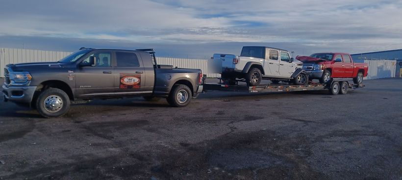 A Jeep and a damaged Silverado loaded on one long trailer