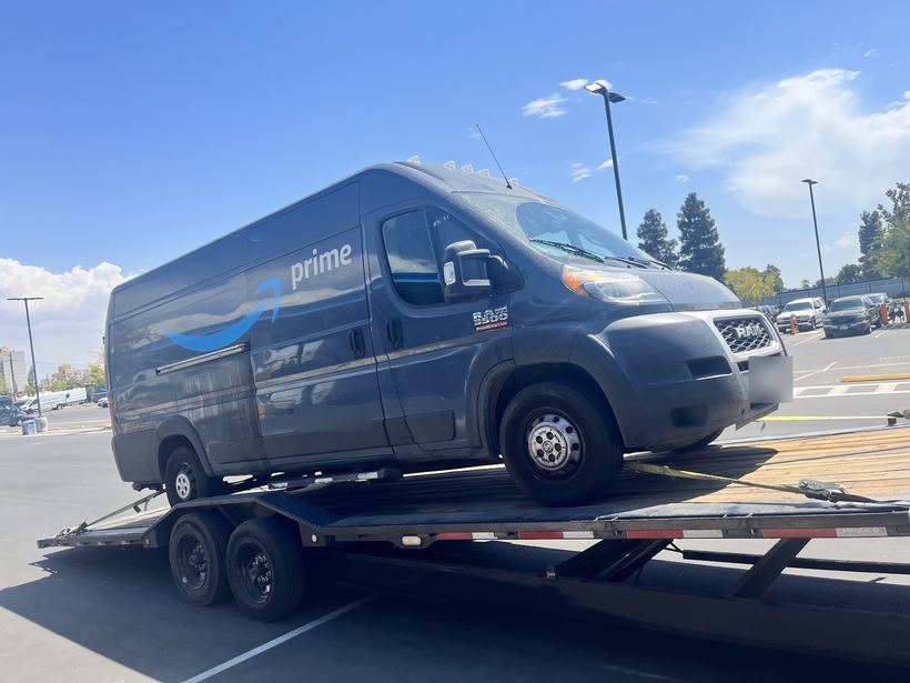 A delivery van strapped onto a flatbed trailer in a parking lot